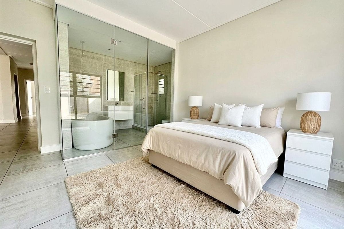 Modern bedroom featuring a sleek glass-enclosed en-suite bathroom with a freestanding bathtub and walk-in shower, complemented by neutral tiled flooring.