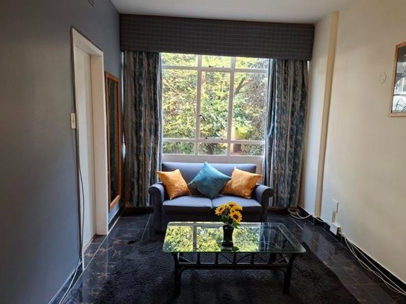 A cozy living room featuring large windows that provide natural light and a view of the garden, complemented by dark tiled flooring.