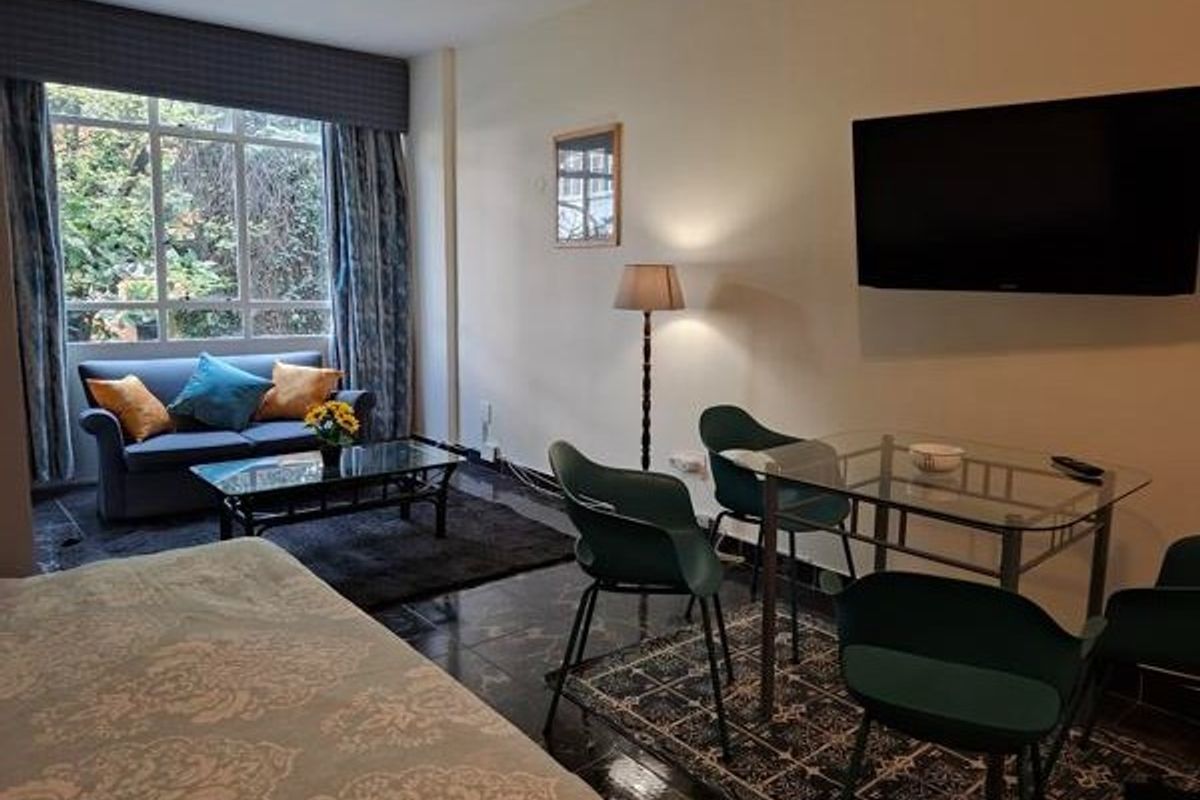 A living area featuring large windows, tiled flooring, and a wall-mounted television, providing a functional space for relaxation and dining.