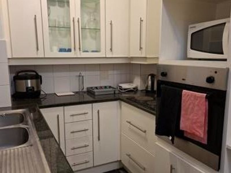 Compact kitchen featuring white cabinetry, dark granite countertops, built-in oven, microwave, and glass-fronted display cabinets.