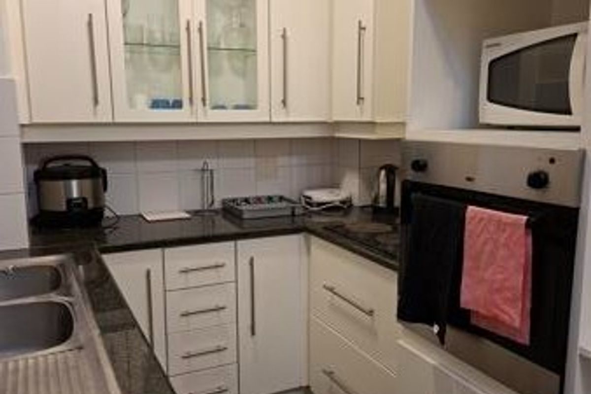 Compact kitchen featuring white cabinetry, dark granite countertops, built-in oven, microwave, and glass-fronted display cabinets.