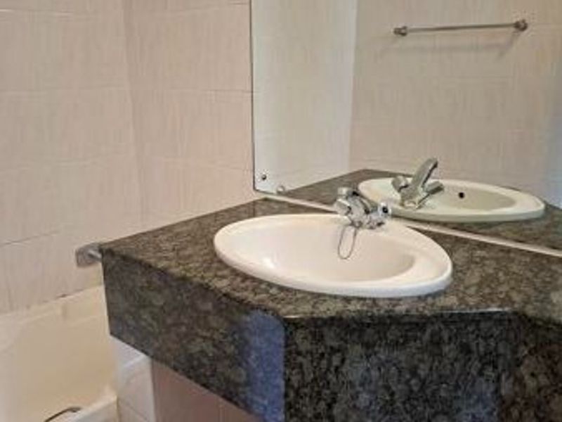 A functional bathroom featuring a granite-topped vanity with a basin, wall-mounted mirror, and a bathtub with tiled wall finishes.