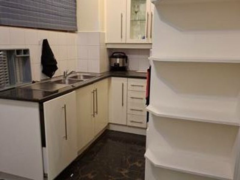 A functional scullery area featuring built-in cabinetry, a stainless steel sink, tiled backsplash, and convenient open shelving for additional storage.