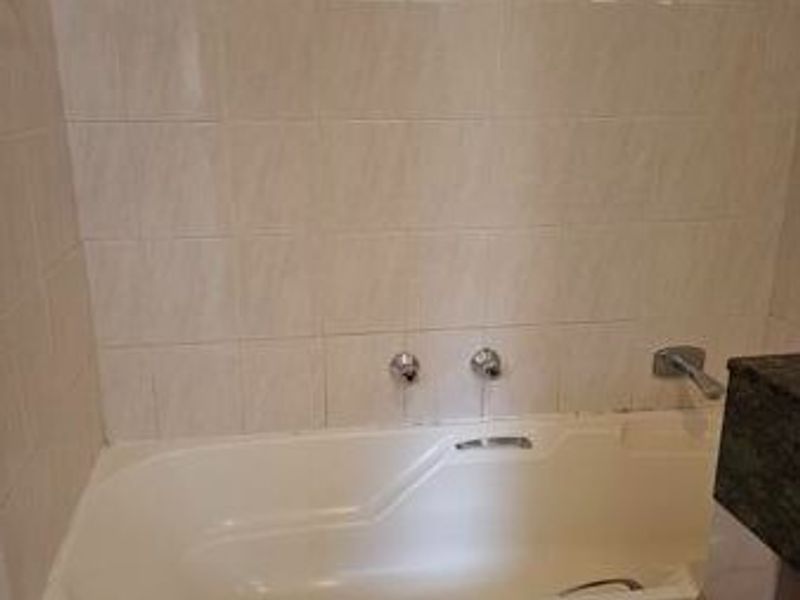 A functional bathroom featuring a built-in bathtub with wall-mounted fixtures and neutral ceramic wall tiling.