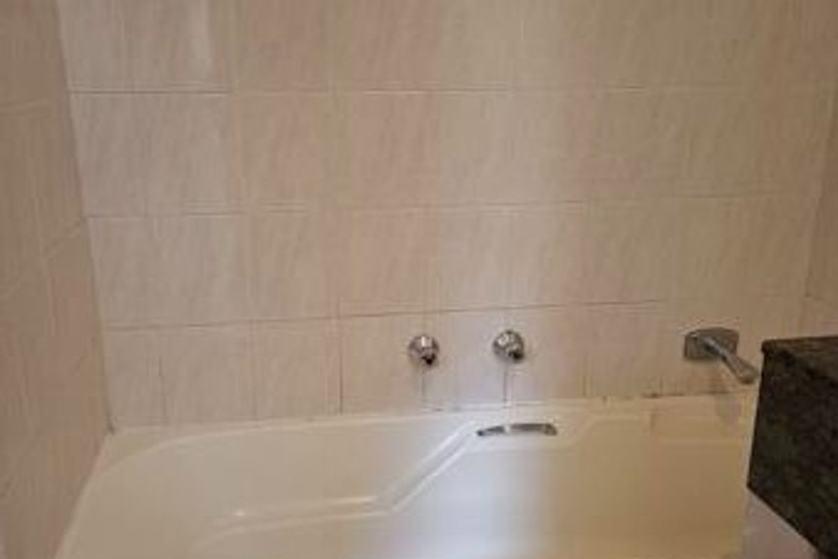A functional bathroom featuring a built-in bathtub with wall-mounted fixtures and neutral ceramic wall tiling.