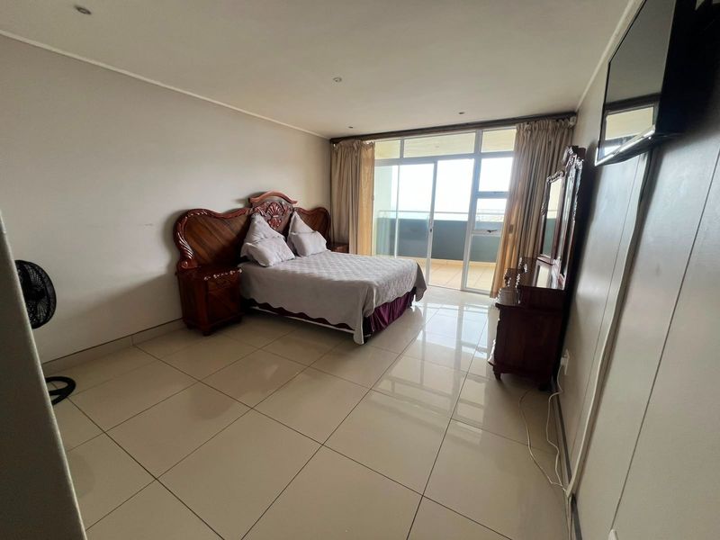 Spacious bedroom featuring large format floor tiles, recessed lighting, and a sliding glass door providing access to a private balcony.