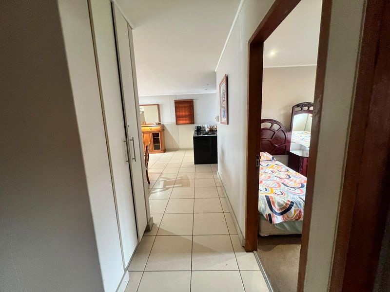 A hallway featuring tiled flooring and built-in storage cupboards, providing access to the adjacent bedroom and open-plan living area.