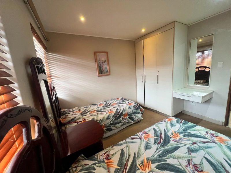 A functional bedroom featuring built-in cupboards, a wall-mounted vanity unit, recessed ceiling lighting, and venetian blinds.