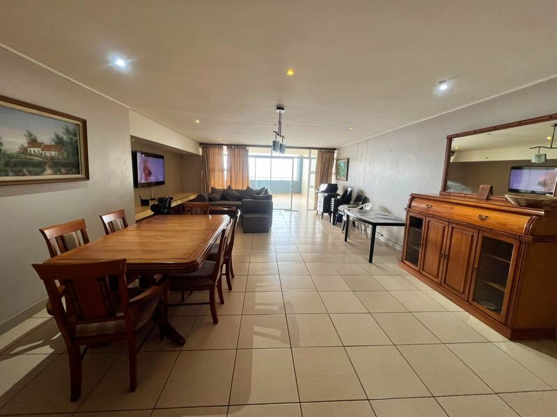 Spacious open-plan living and dining area featuring neutral ceramic floor tiles, recessed lighting, and direct access to a balcony through sliding glass doors.