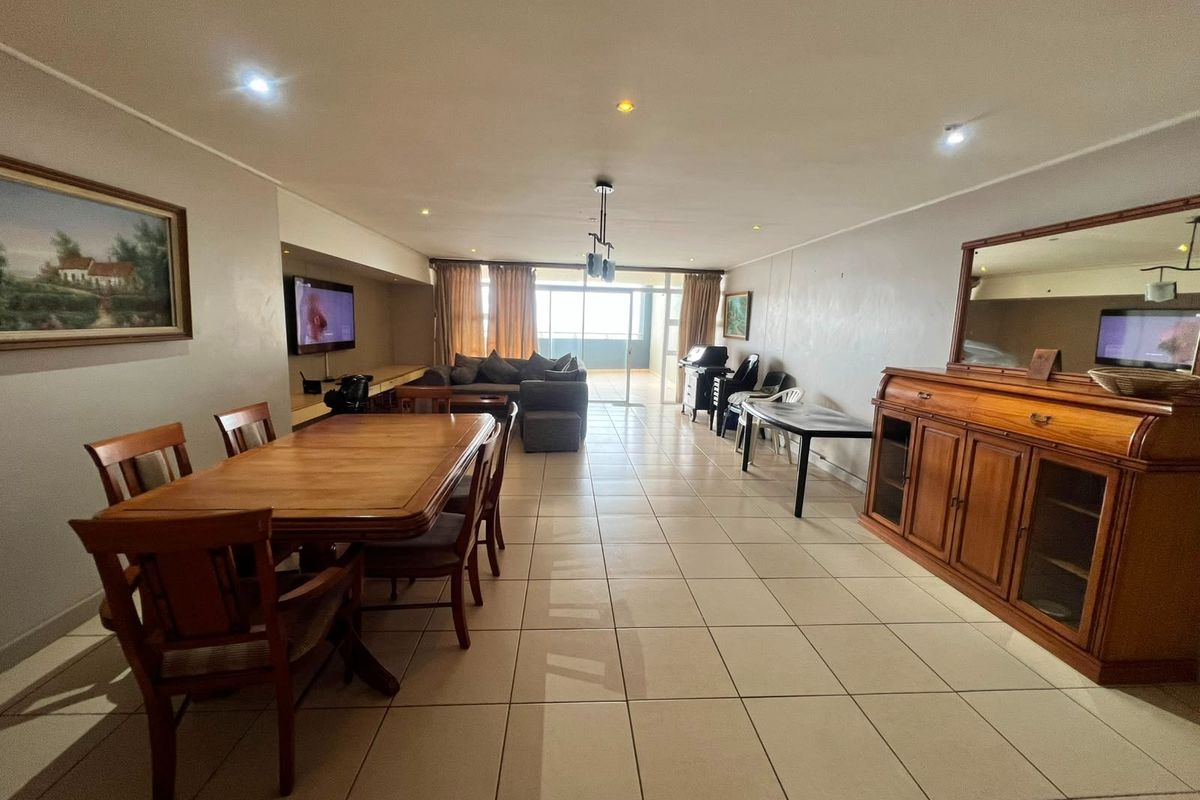 Spacious open-plan living and dining area featuring neutral ceramic floor tiles, recessed lighting, and direct access to a balcony through sliding glass doors.