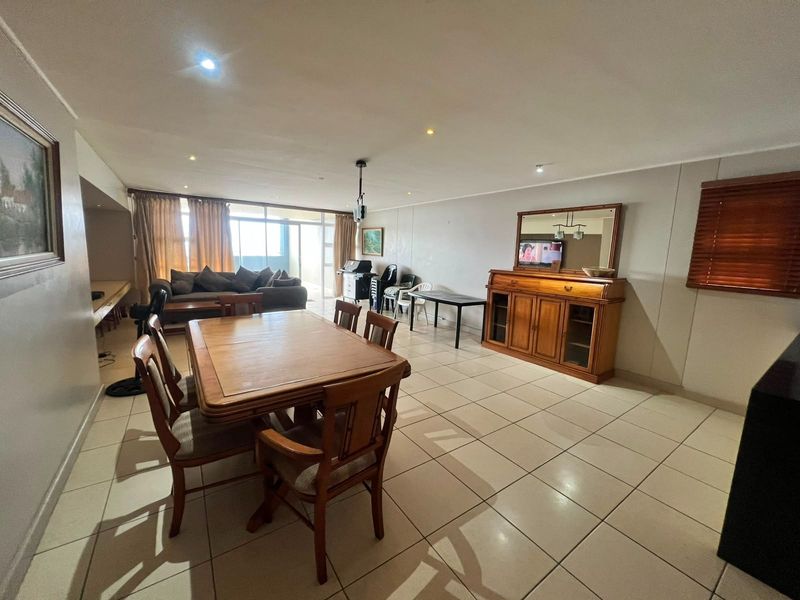 Spacious open-plan living and dining area featuring neutral tiled flooring, recessed lighting, and large sliding glass doors leading to an outdoor space.