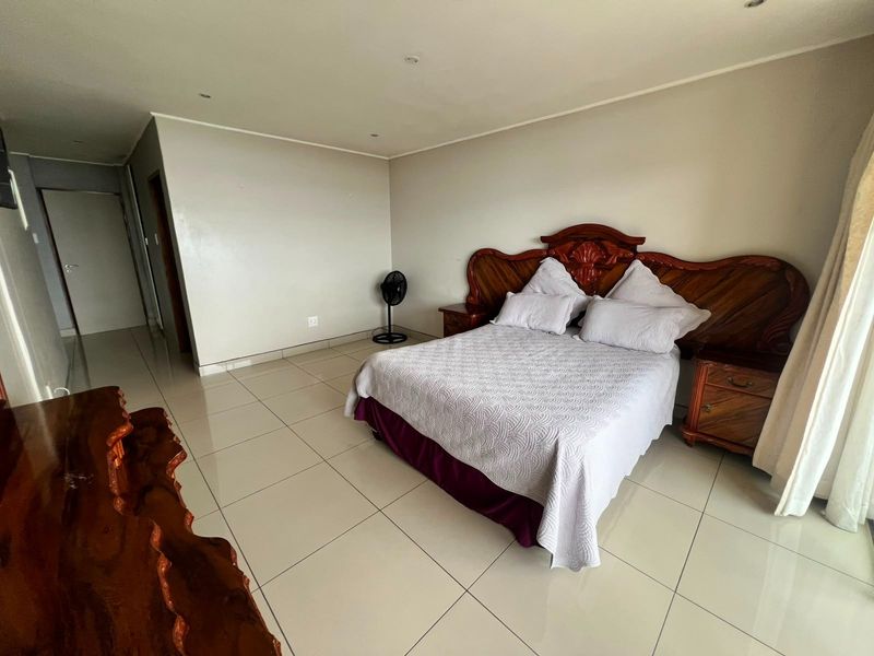 A spacious bedroom featuring neutral wall tones, large format floor tiles, and recessed downlighting, offering a clean and functional living space.
