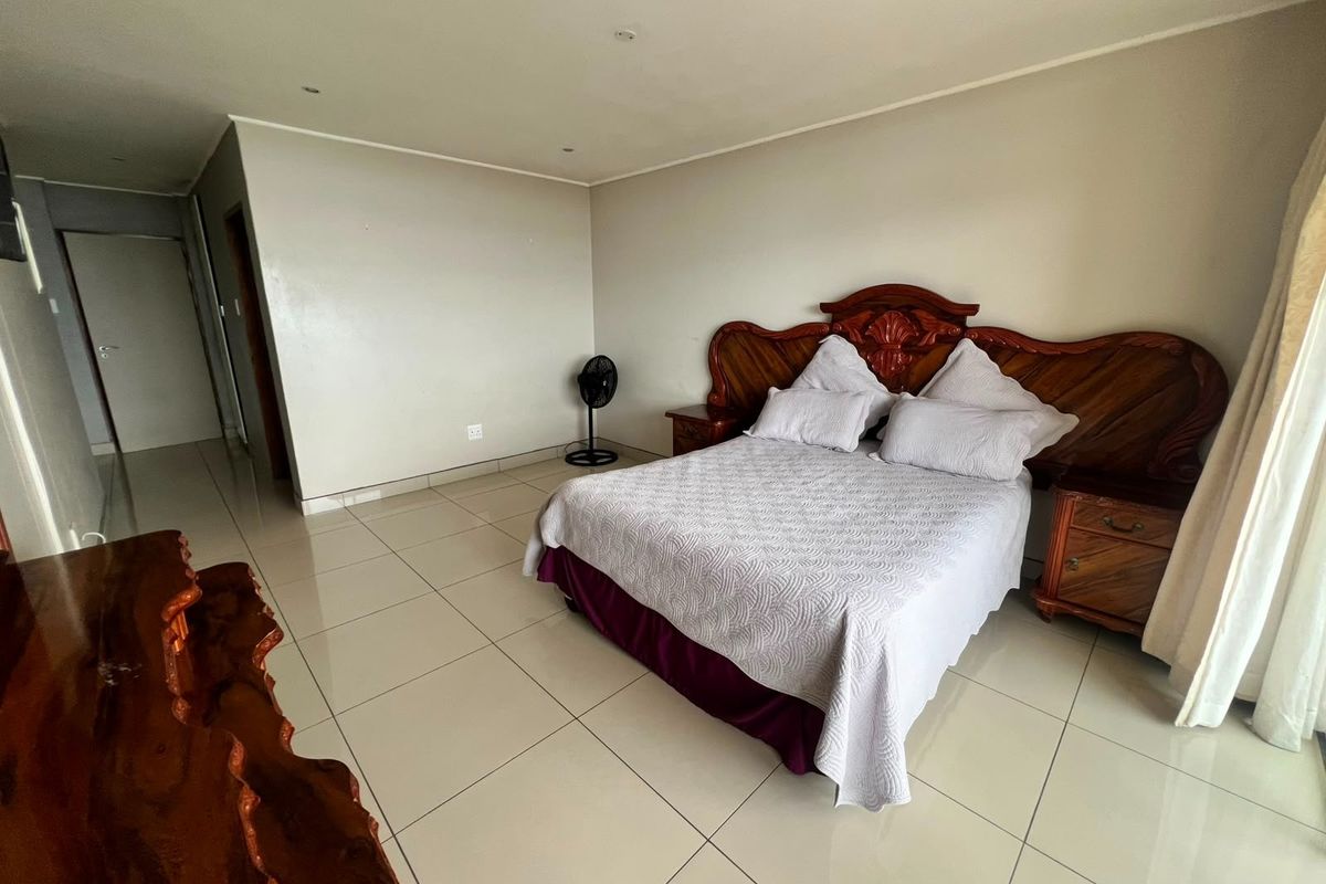 A spacious bedroom featuring neutral wall tones, large format floor tiles, and recessed downlighting, offering a clean and functional living space.