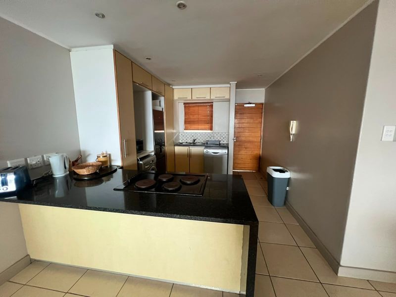 A functional kitchen featuring granite countertops, built-in cabinetry, an electric hob, and tiled flooring, providing a practical layout for daily meal preparation.