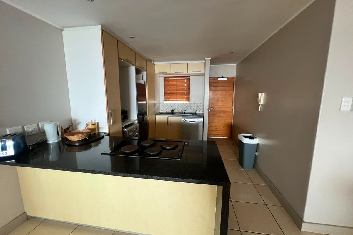 A functional kitchen featuring granite countertops, built-in cabinetry, an electric hob, and tiled flooring, providing a practical layout for daily meal preparation.