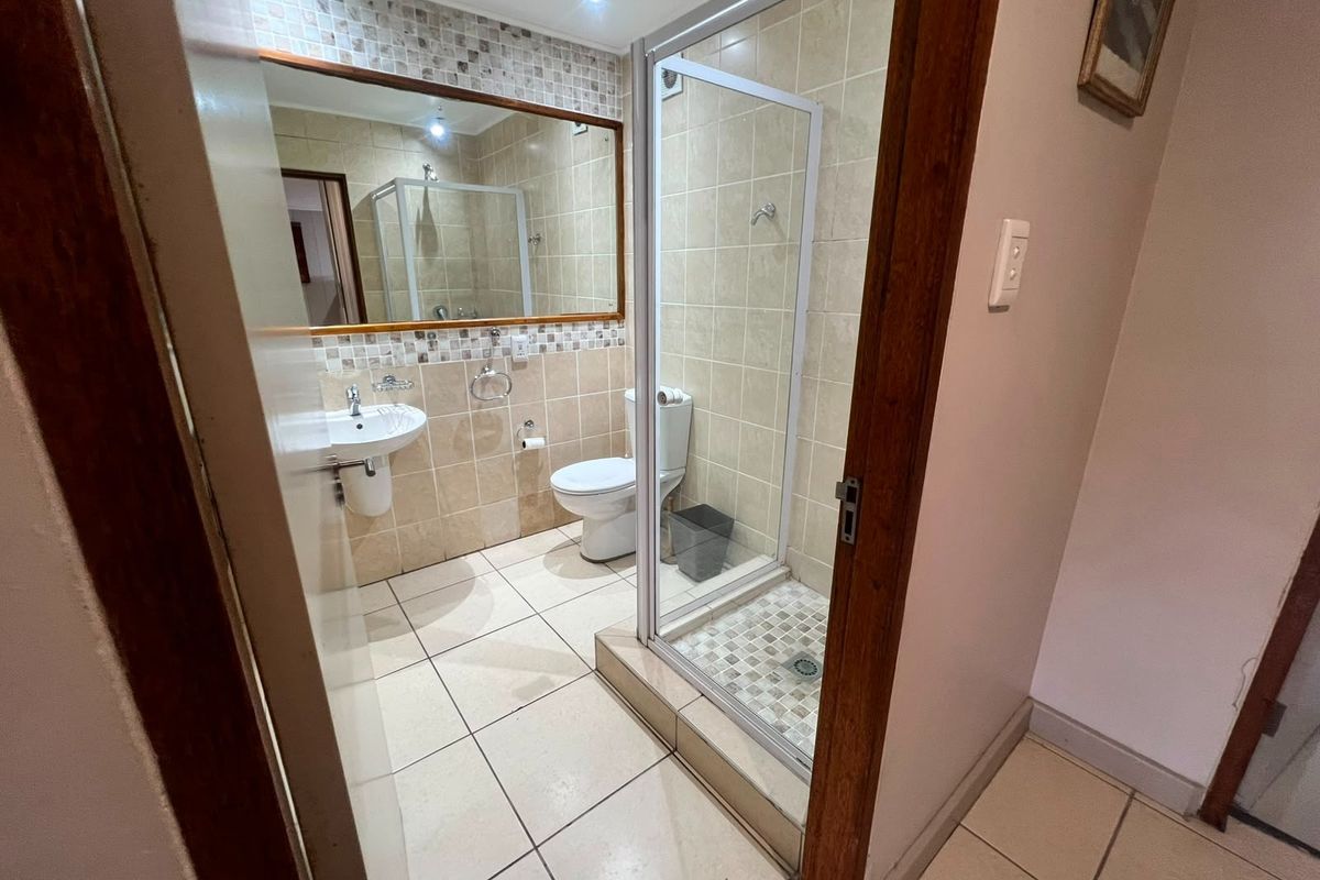 A clean and functional bathroom featuring a glass-enclosed shower, pedestal basin, toilet, and neutral wall and floor tiling.