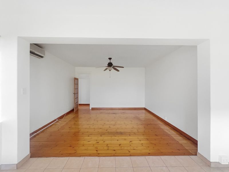 An empty living room featuring polished timber flooring, a ceiling fan, and a wall-mounted air conditioning unit, providing a blank canvas for interior design.