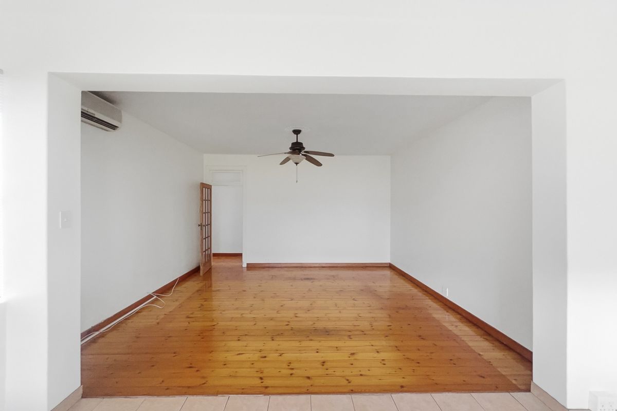 An empty living room featuring polished timber flooring, a ceiling fan, and a wall-mounted air conditioning unit, providing a blank canvas for interior design.