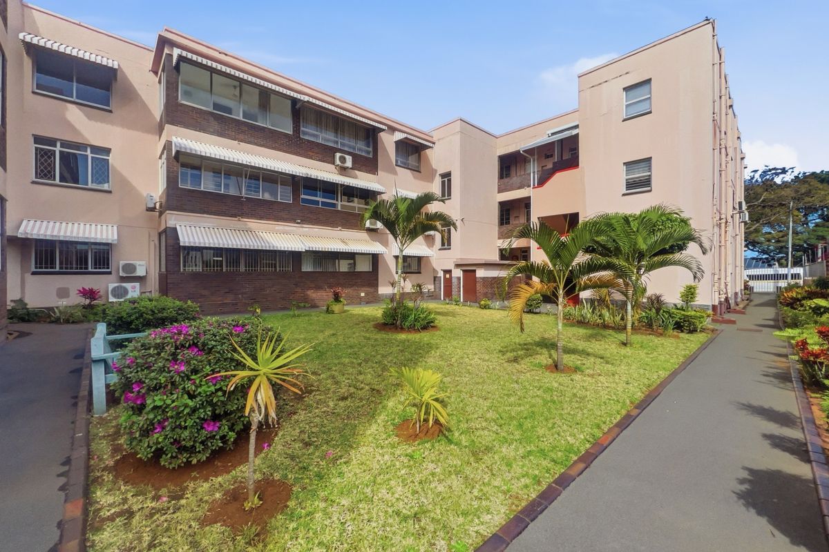 Rear view of the apartment complex featuring a well-maintained communal garden, paved walkways, and brick facade with window awnings.