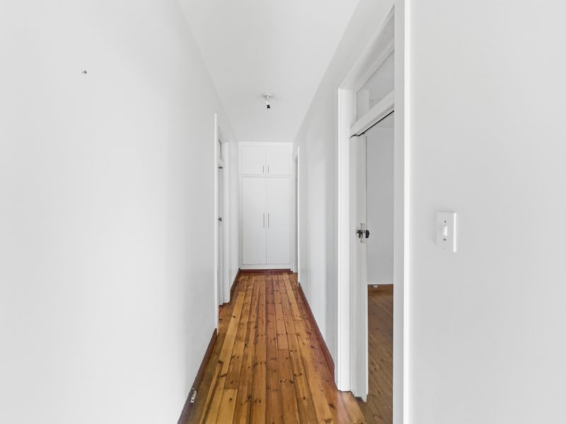A bright, empty hallway featuring polished hardwood flooring and a built-in storage cupboard at the end, providing clean access to adjacent rooms.