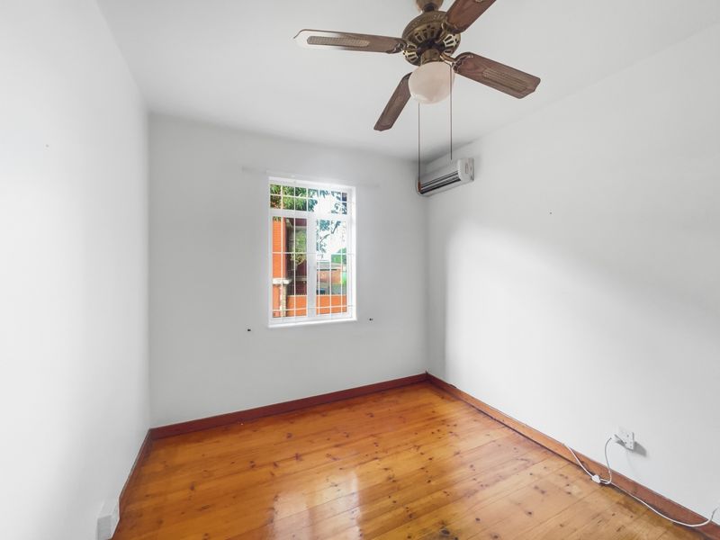 An empty bedroom featuring polished timber flooring, a ceiling fan, and a wall-mounted split-system air conditioning unit.