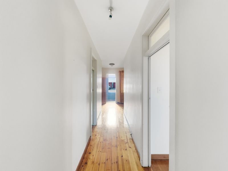 A bright, empty hallway featuring polished timber flooring and neutral wall finishes, providing access to multiple rooms within the apartment.