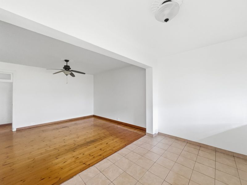 An empty open-plan living area featuring a combination of polished hardwood and ceramic tile flooring with a ceiling fan.