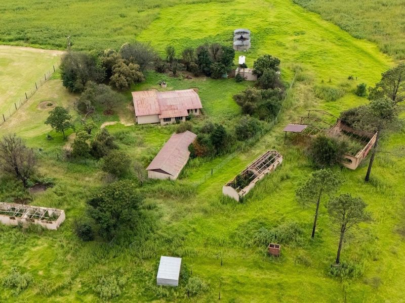 Aerial view of a farm property featuring a main farmhouse, multiple outbuildings in various states of repair, and surrounding agricultural land.