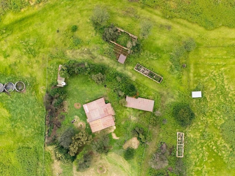 Aerial view of a rural farm property featuring multiple outbuildings, water storage tanks, and fenced enclosures set within expansive green pasture land.