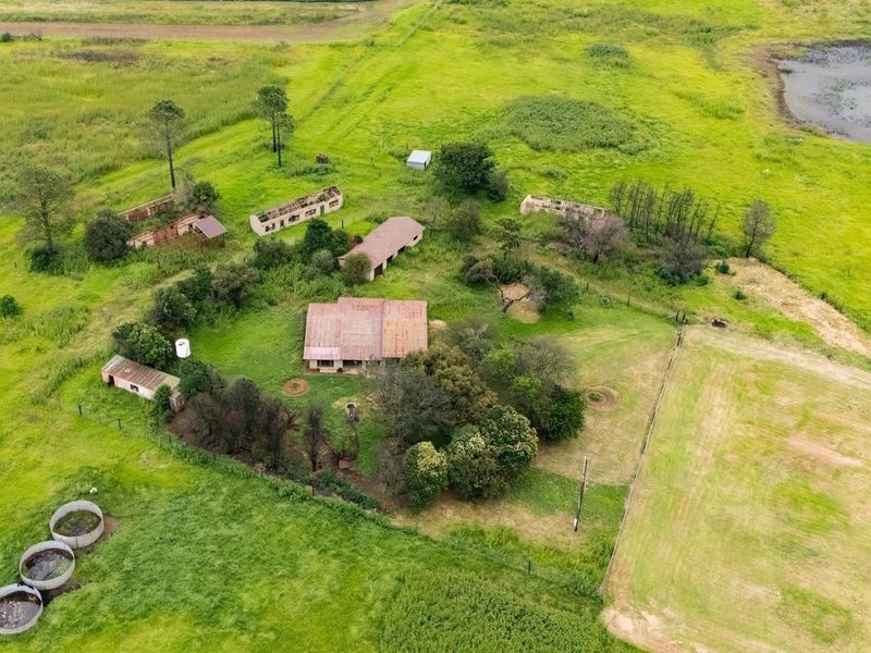 Aerial view of a farm property featuring a main residence, several dilapidated outbuildings, water storage tanks, and expansive surrounding agricultural land.