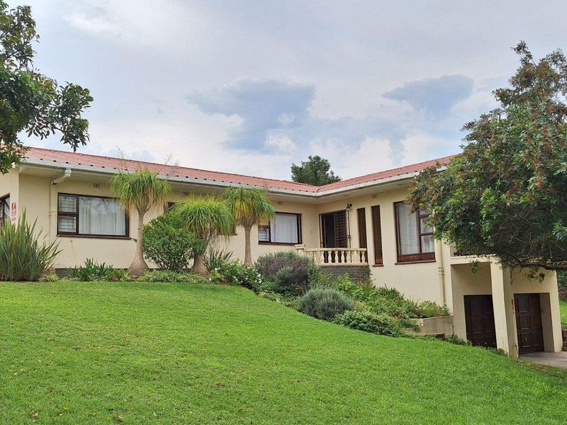 A well-maintained single-story residential property featuring a tiled roof, established garden, and integrated garage, set on a spacious sloped lawn.