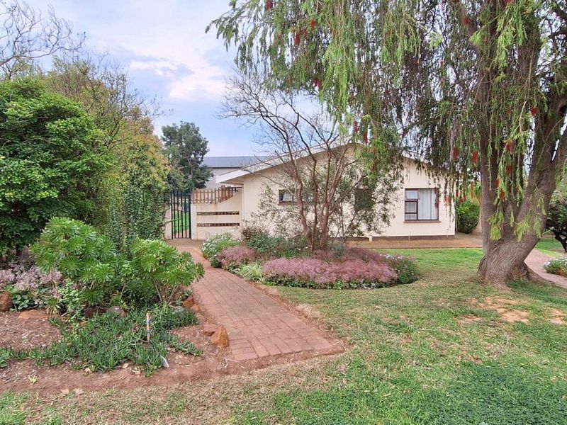 A well-maintained front garden featuring a brick paved pathway leading to the entrance of the house, surrounded by mature trees and established landscaping.