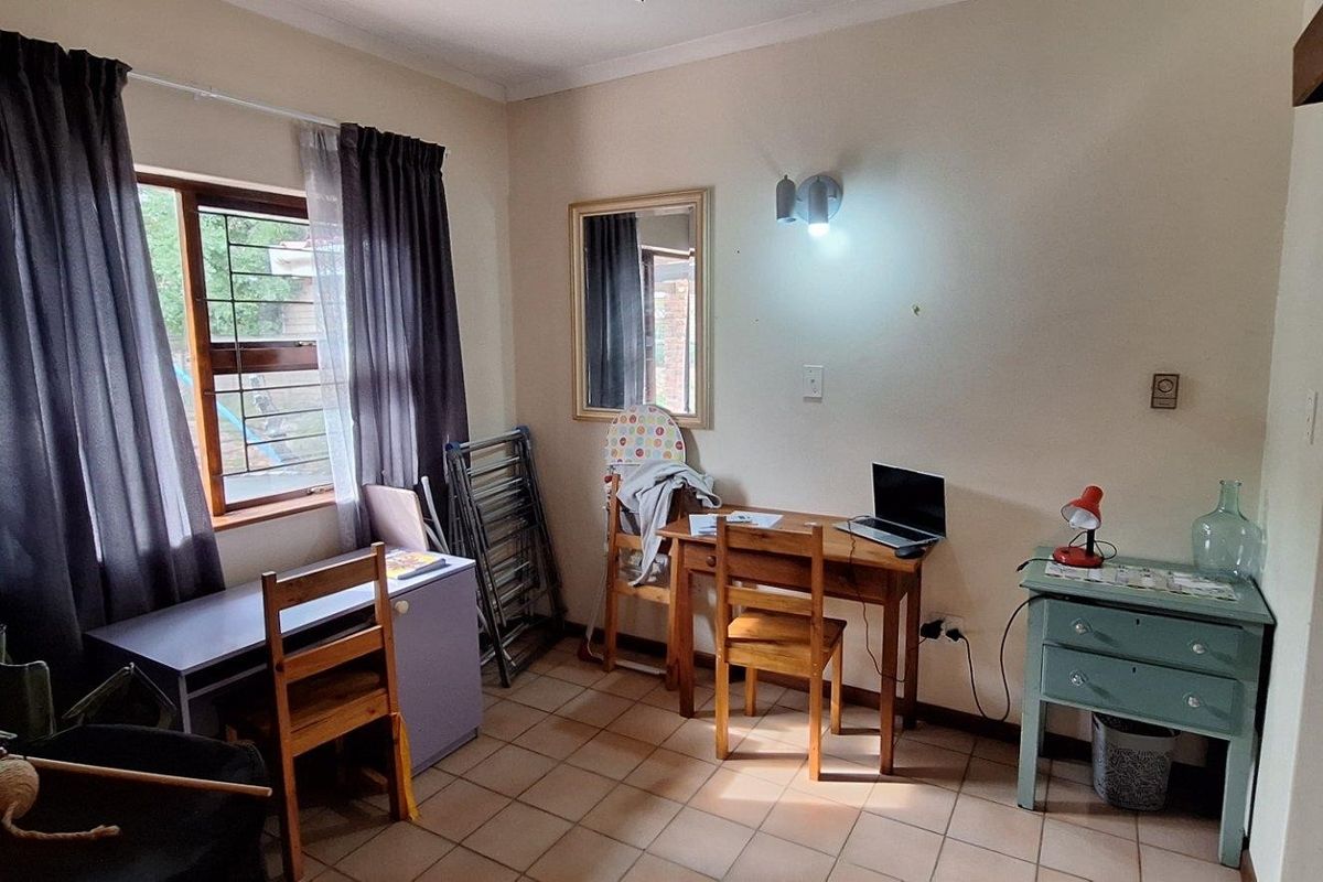A functional bedroom featuring tiled flooring and a window with security bars, providing a practical space for a home office or study area.