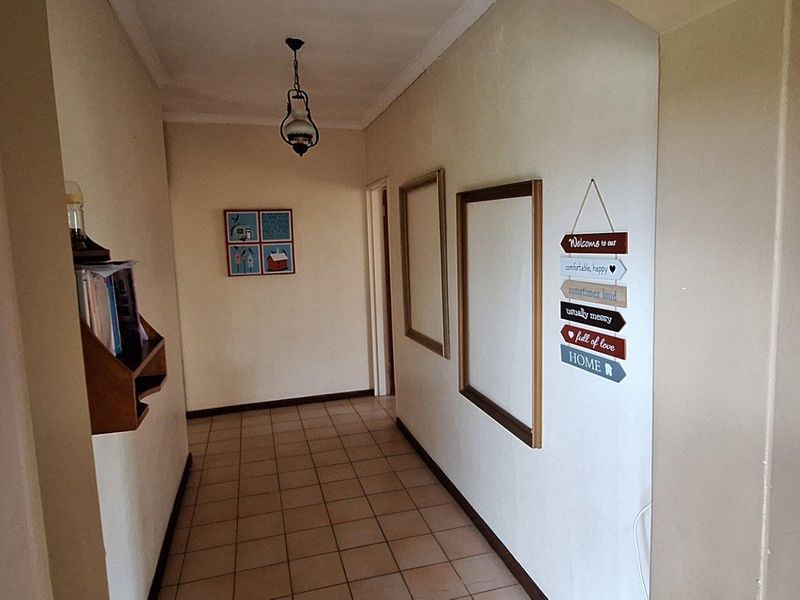 A functional hallway featuring tiled flooring, neutral wall finishes, and a central pendant light fixture, providing access to adjacent rooms.