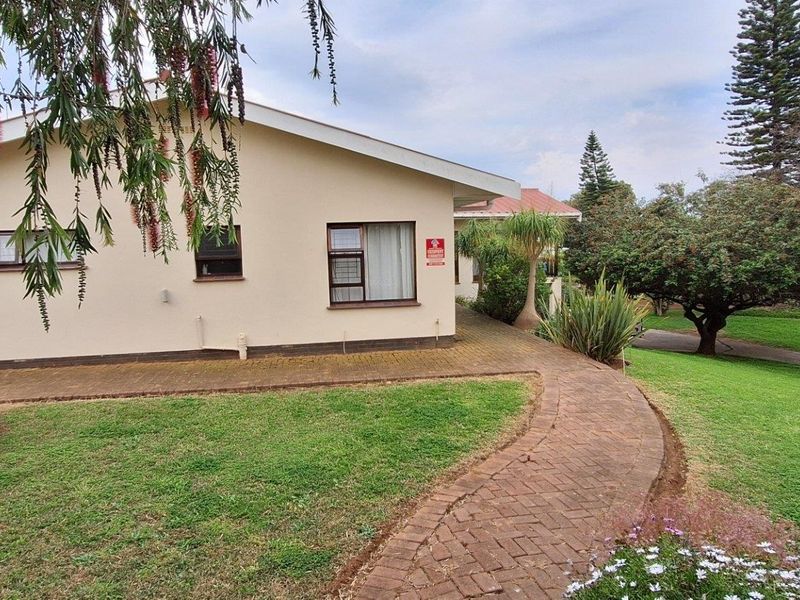 A well-maintained rear exterior view of the house featuring a paved walkway, brick patio area, and established garden landscaping.