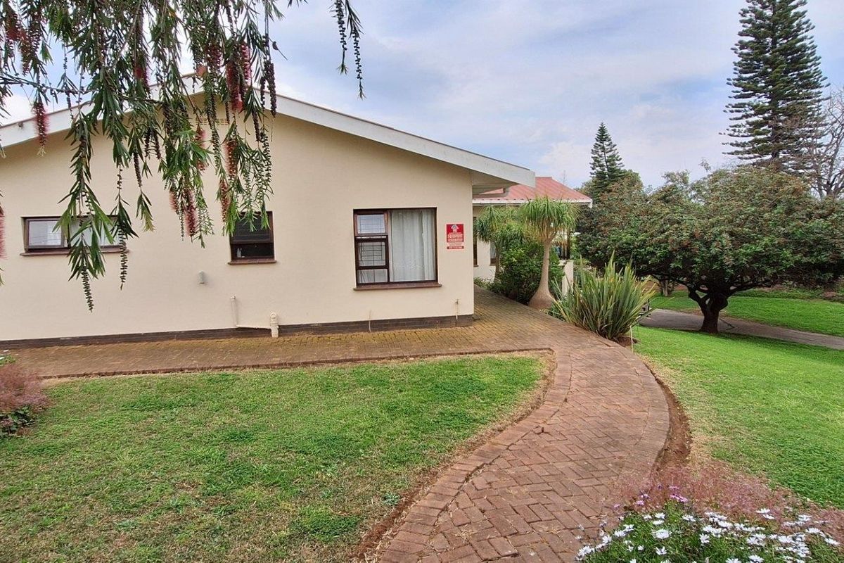 A well-maintained rear exterior view of the house featuring a paved walkway, brick patio area, and established garden landscaping.