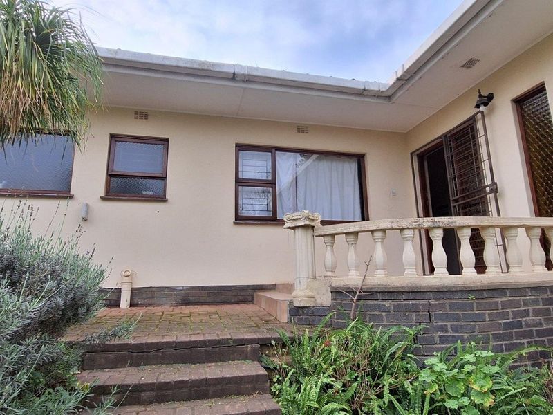 Rear exterior view featuring a brick patio with steps, a concrete balustrade, and aluminium window frames, showing signs of age and wear.