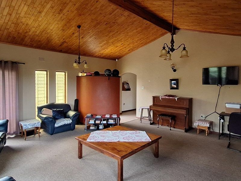 Spacious living room featuring a vaulted timber ceiling, brick fireplace, and unique glass block windows, offering a warm and character-filled living space.