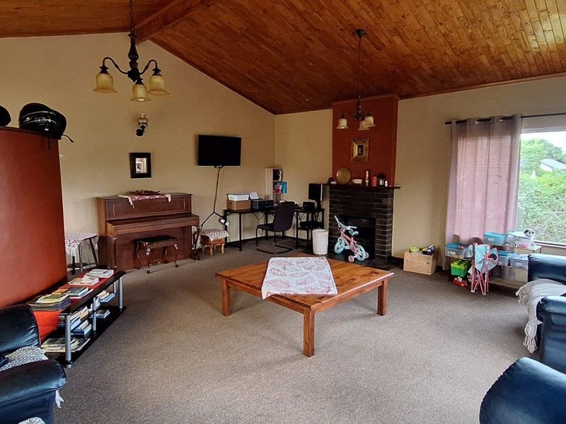 Spacious living room featuring a vaulted timber ceiling, a classic brick fireplace, and large windows providing natural light.