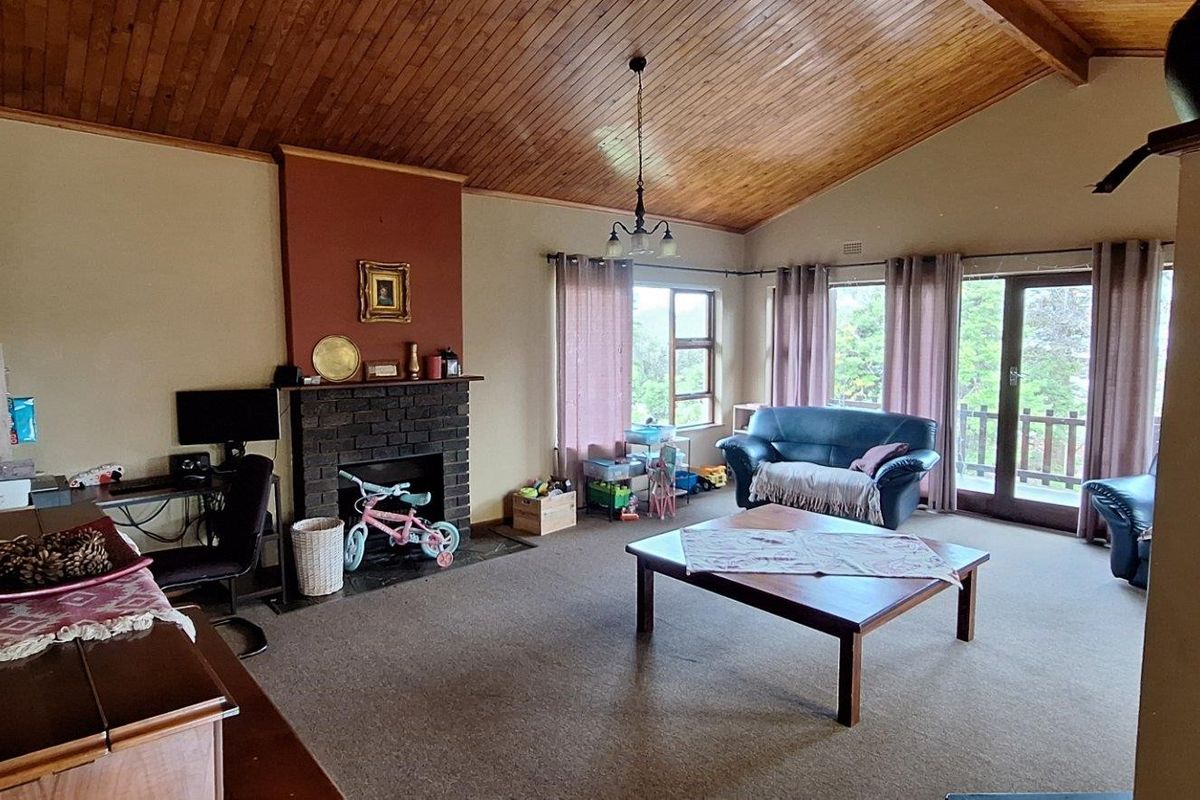 Spacious living room featuring a vaulted timber ceiling, a brick fireplace, and sliding glass doors leading to an outdoor area.
