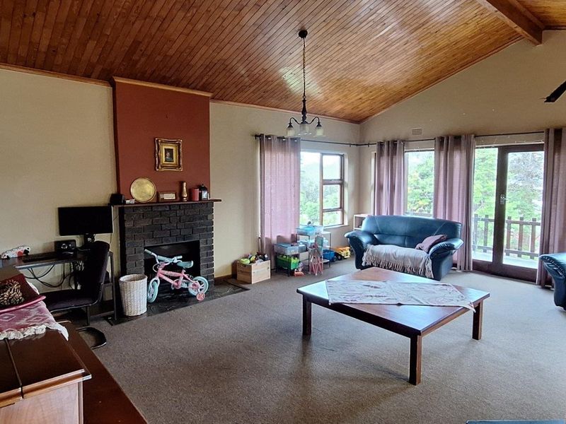 Spacious living room featuring a vaulted timber ceiling, a brick fireplace, and sliding glass doors leading to an outdoor area.