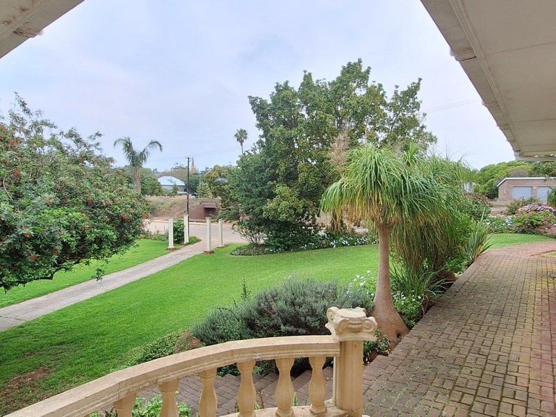 A covered patio area featuring a paved walkway and balustrade, overlooking a well-maintained garden and surrounding neighborhood.