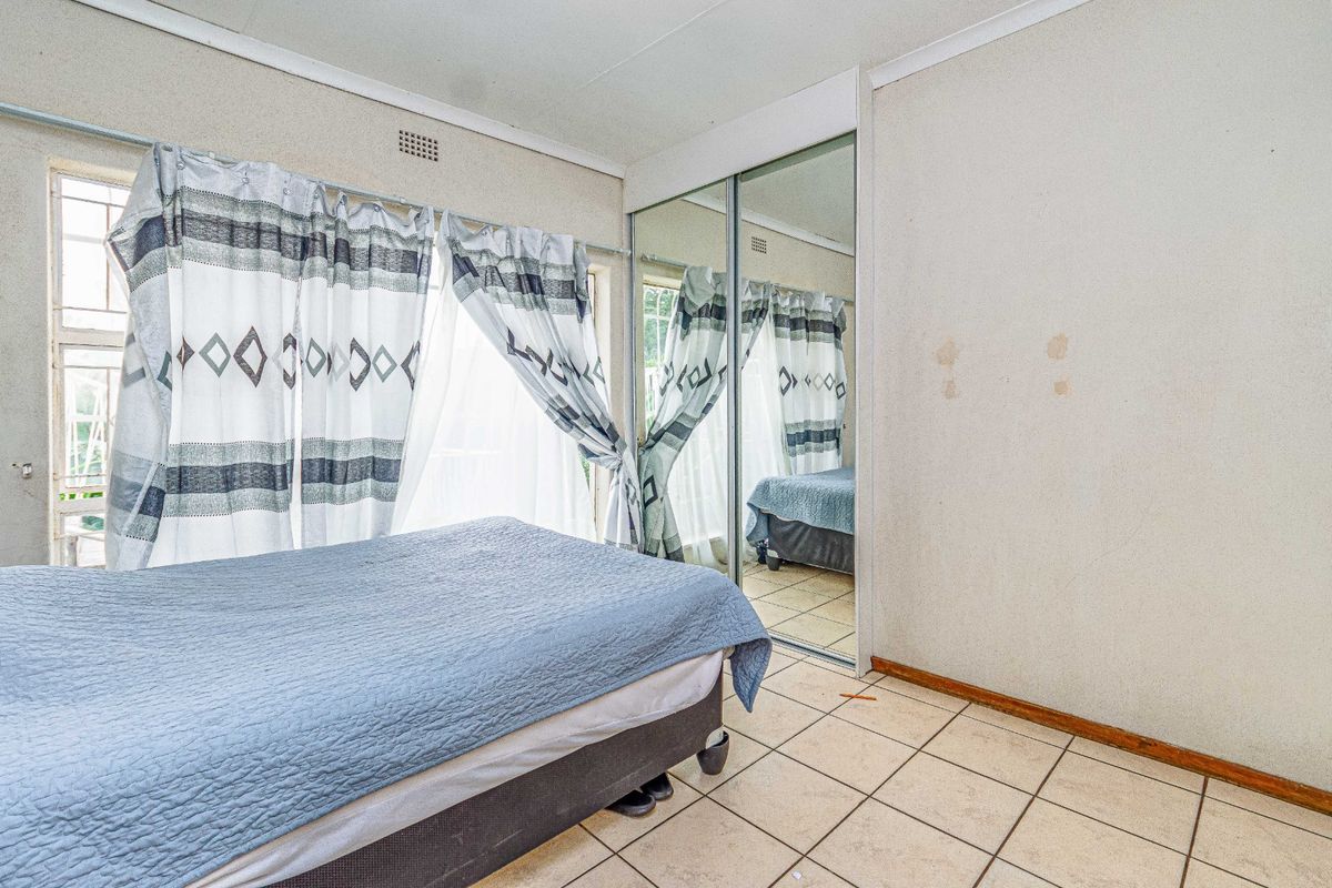 A bedroom featuring tiled flooring, a built-in mirrored wardrobe, and a window with security bars. The room requires cosmetic wall repairs.