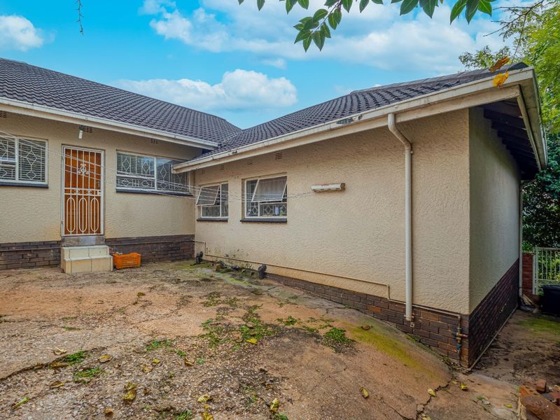 Rear exterior view of the house featuring a tiled roof, security gates, and a concrete patio area requiring maintenance.
