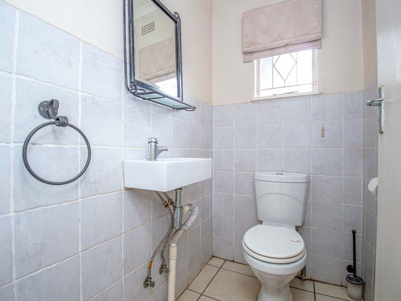 A compact guest bathroom featuring a wall-mounted basin, toilet, and neutral tiled finishes throughout.