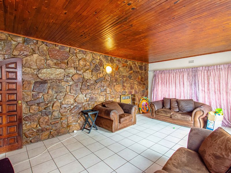 Living room featuring a prominent stone feature wall, timber-clad ceiling, and ceramic tiled flooring with a built-in wall heater.