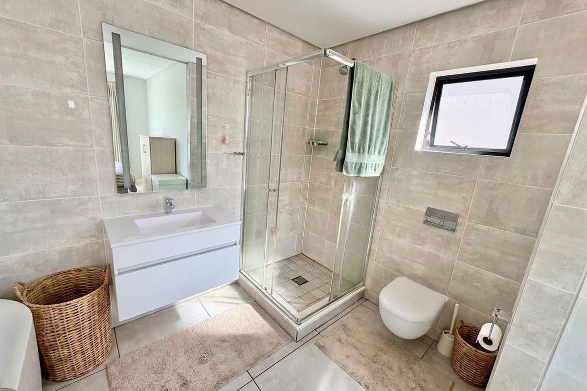 Modern bathroom featuring a wall-mounted vanity with integrated basin, glass shower enclosure, and wall-hung toilet with concealed cistern, finished with neutral wall and floor tiles.