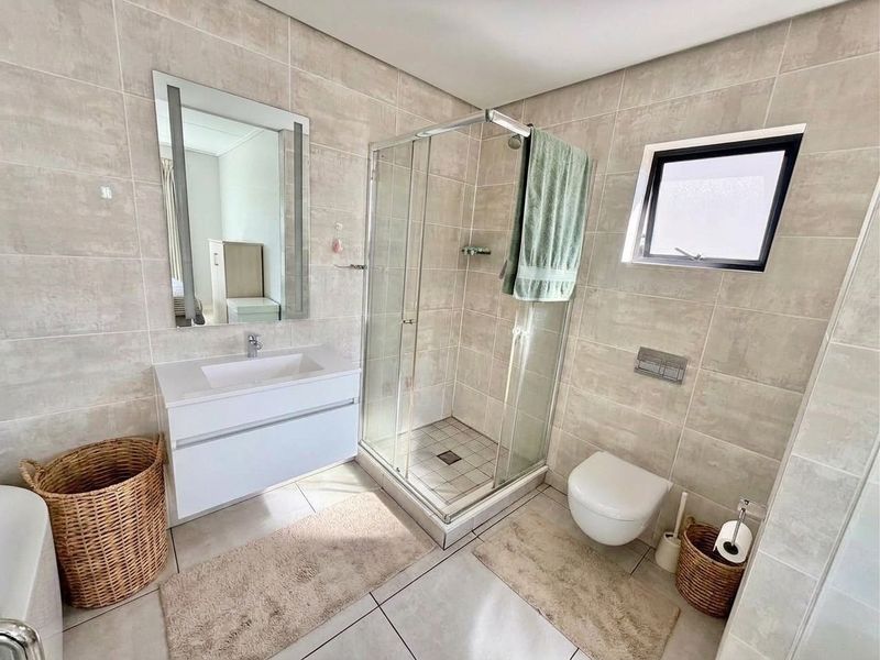 Modern bathroom featuring a wall-mounted vanity with integrated basin, glass shower enclosure, and wall-hung toilet with concealed cistern, finished with neutral wall and floor tiles.