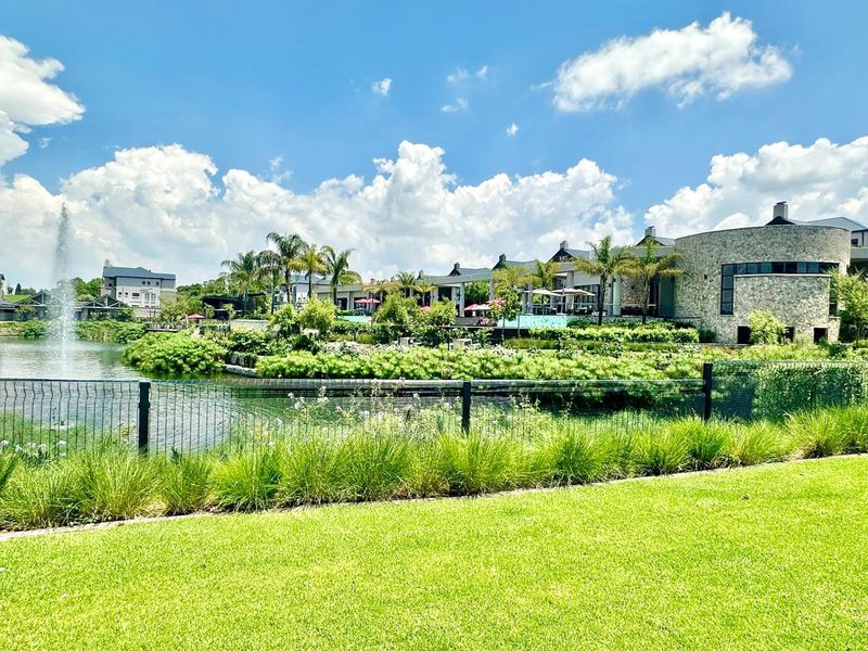 A scenic view of a landscaped garden, pond with a water feature, and the stone-clad exterior of the estate clubhouse.