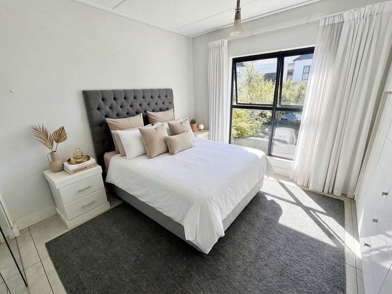 A bright and well-maintained bedroom featuring tiled flooring, a large black-framed window with natural light, and built-in wardrobe storage.